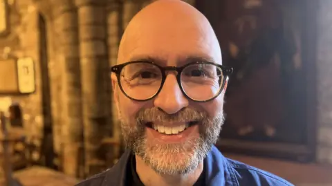 Bald man with beard and moustache smiling at the camera in St Germans Priory