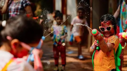 Reuters A girl sprays her friend with water during holi celebrations in Mumbai, India, March 14, 2025.