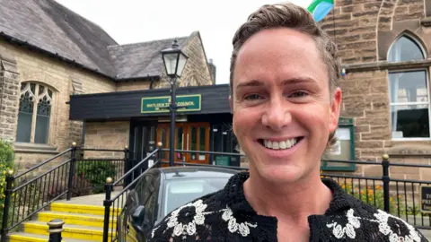 Image of Ashley Orwin. He is smiling for the camera and is stood in front of Matlock Town Council.