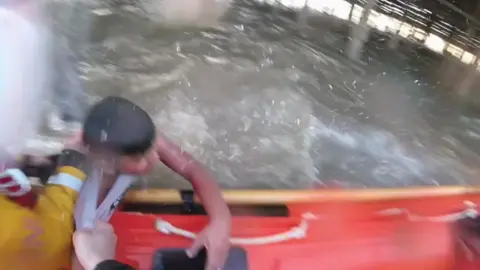 Image shows a boy being dragged from the water into a lifeboat