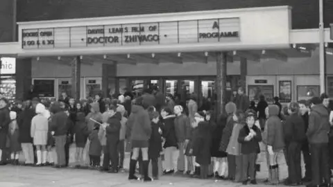 Harlow Council A black and white photograph showing a long line of people queuing to get into the old Odeon cinema when it was open.