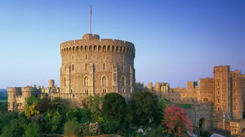 Image of Windsor Castle from a distance with green and red trees in front of it