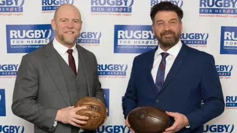 Getty Images Mike Tindall and Nick Knowles pose with rugby balls against a backdrop at an event