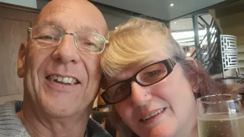 Steven and Julie Murfin pose for a selfie. They both wear glasses and their heads touch as they lean forward together