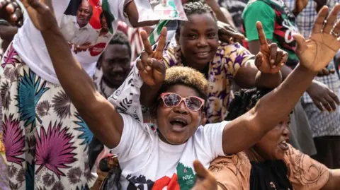 AFP A supporter of former Ghana President wearing sunglasses and raising their hands in excitement - 8 December 2024.