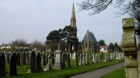 Rows of tombstones in a graveyard with a church building in the background.