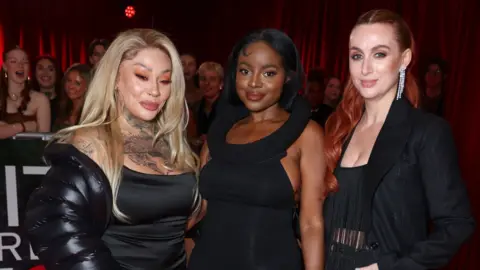 Sugababes stand on a red carpet at the Brit Awards 2025, they are all wearing black