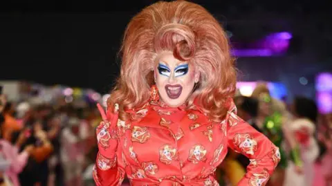 Getty Images Drag artist Porkchop with a red outfit on and wearing a large red wig with blonde streaks.