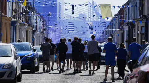 PA Media Silhouetted fans take their usual walk through city streets to the ground, pictured in the background