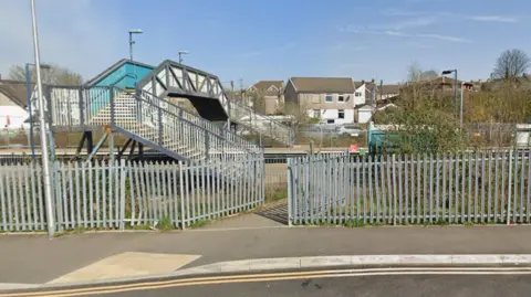 A view of Pontyclun train station with a fence around an entry route to the platform. There is a bridge going over the tracks.
