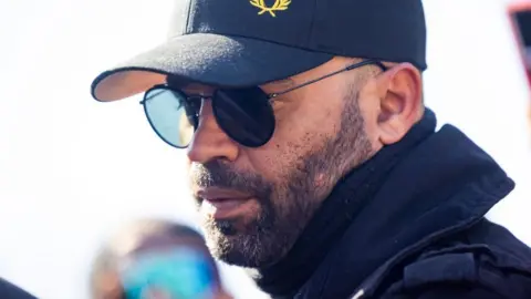 Headshot of Enrique Tarrio wearing sunglasses and a cap