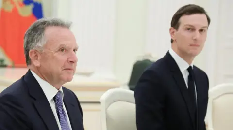 Reuters Steve Witkoff and Jared Kushner, both wearing dark suits, look across a negotiating table in the Kremlin. In the background is a draped Russian flag. 