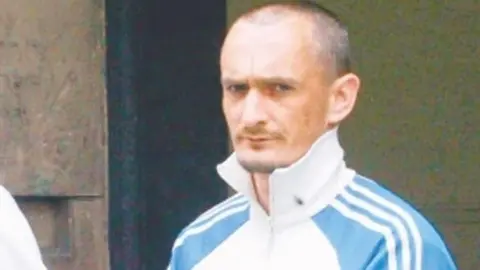 A man with short hair and wearing a blue tracksuit top 