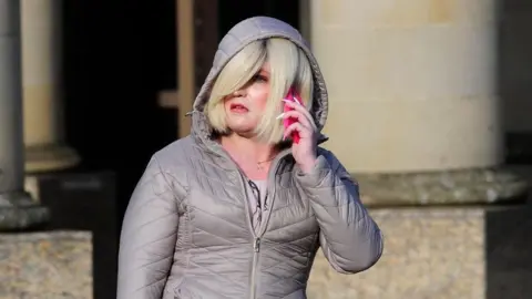 Spindrift Isla Byrson, with blonde hair and a grey hooded jacket, speaks on the phone outside court. 