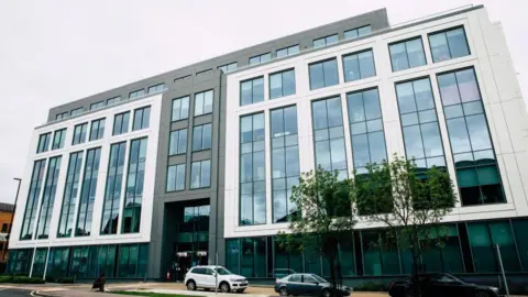 The Slough Borough Council building, a glass building with trees and parked cars outside.