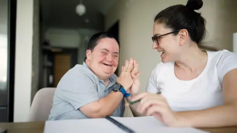 Getty Images A man laughs with his female support worker while they are both sat at a desk with a pen and paper 