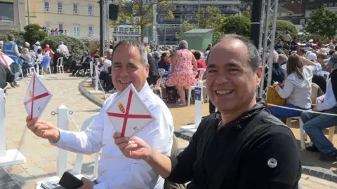 idential twin brothers smile and wave Jersey flags in a busy ceremony setting