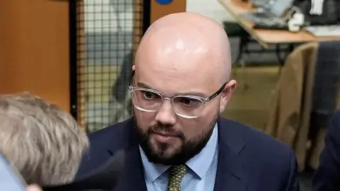 PA Media Llyr Powell, in blue suit, surrounded by people with cameras and microphones. 