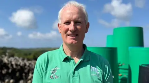 Ray Cox has short grey hair and is wearing a green polo shirt with Parish Walk embroidered onto the right side.
