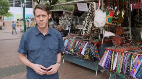 BBC correspondent Will Grant standing in front of market stall