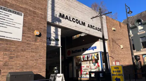 A brick shopping centre entrance with a large black and white sign above it saying Malcolm Arcade