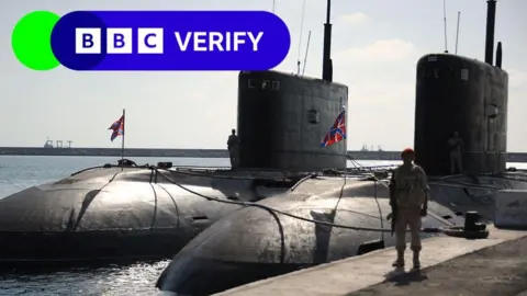 Getty Images Russian submarines docked in Tartous in 2019. An armed soldier stands next to the vessels on a dock. 