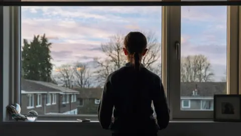 A child in silhouette looks out of a window