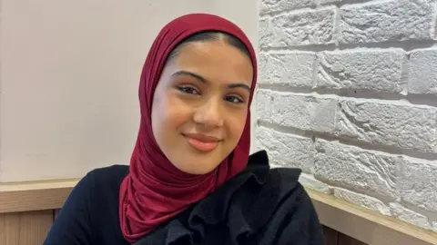Zaynah wearing a burgundy headscarf and black top 