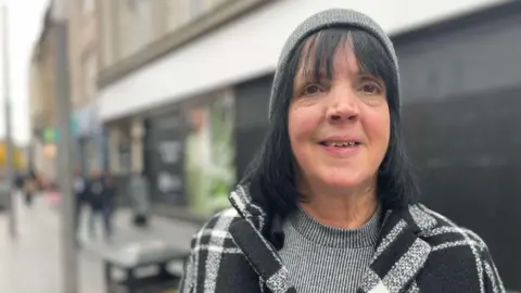 A woman in a beanie hat, gray jumper and monochrome coat outside a closed M&S store in Leicester