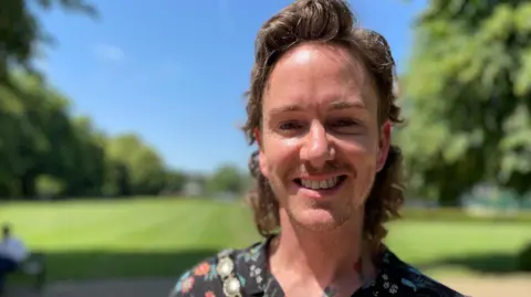 BBC Man in his thirties with shoulder-length hair in a sunny park