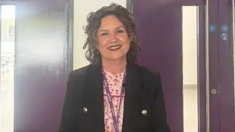 A woman is smiling near two sets of purple double doors.