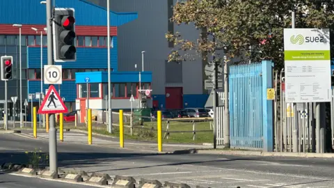 The entrance to Haverton Hill recycling centre in Billingham. Large grey and blue buildings stand at the end of a road. A sign says the site is operated by Suez.
