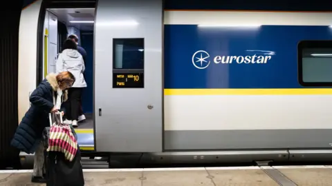 Getty Images A woman gets onboard a stationary Eurostar train. She is holding a suitcase and a multicoloured tote bag