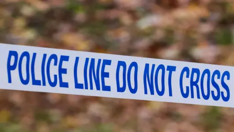 White police tape which reads 'POLICE LINE DO NOT CROSS' in blue letters. The background is blurred.