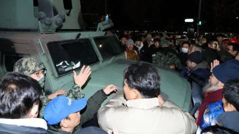 EPA-EFE People crowd around a military vehicle in front of the National Assembly building