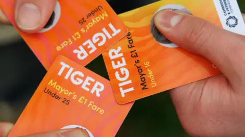 Three orange cards which say 'Tiger Mayor's £1 Fare' A persons thumb covers a photograph on each card. 