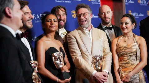 Getty Images Peter Huyck, Frida Perez, James Weaver, Seth Rogen, Evan Goldberg and Chase Sui Wonders standing together, smiling and talking, holding their Baftas