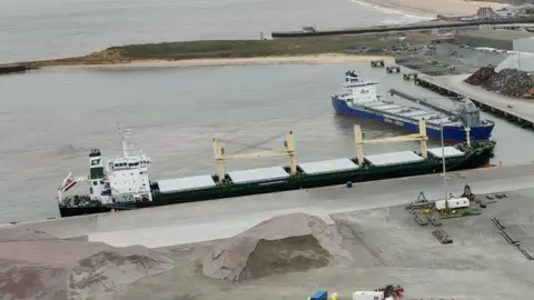 A container ship with four large cranes berthed at a dock