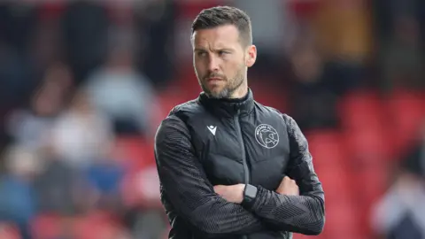Walsall boss Mat Sadler looks pensive as he stands with arms folded watching from the touchline 