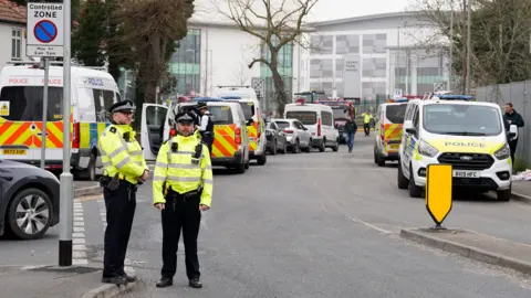 Police officers stand beside numerous police vans on a road