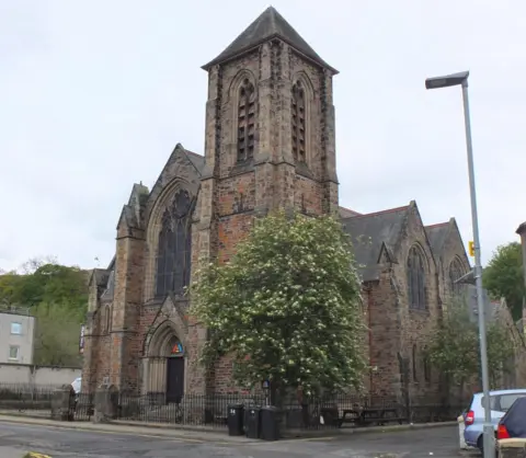 Jim Barton A large church building with a tall tower and a tree growing in front