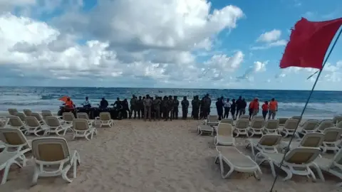 Defensa Civil Dominicana Officials in military and officials uniforms search the beach, which is full of empty beach chairs, for Sudiksha Konanki