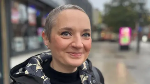 BBC Lucy Shannon is standing on the high street and smiling at the camera. She has short grey hair.