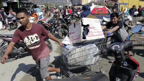 EPA People drag a shopping trolley with goods looted from a supermarket in Palu. Photo: 30 September 2018