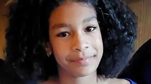Candid photo of Kaliyah Coa, who died after falling into the Thames. She is 11 and is wearing a blue top and smiling at the camera with big brown eyes and curly hair.