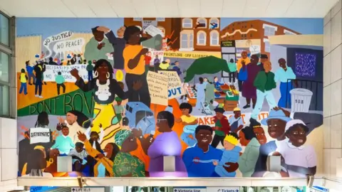 Angus Mill The vibrant mural featuring many people hangs on a pale tiled wall.