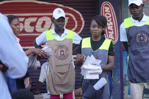Electoral officers handle ballot papers on voting day in Uganda.
