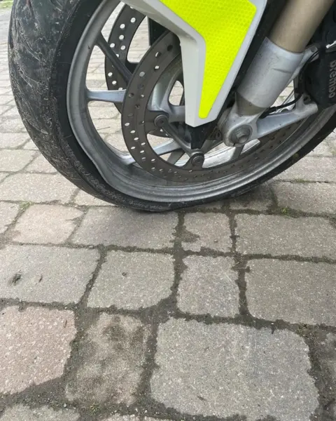 Warwickshire and Solihull Blood Bikes A close-up of a motorbike tyre which has deflated. The middle of the wheel is yellow to match the rest of the bike, and the tyre is on a bricked surface.