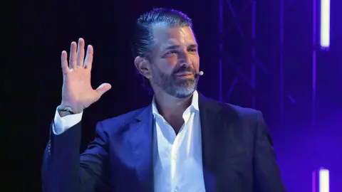 Getty Images A man in a suit, waving one hand and looking off-camera to the right
