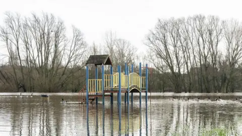 Ian Knight / Z70 Photography Water surrounds a construction in the middle of the photo that has about a dozen blue poles and yellow railings. Trees are in the background.